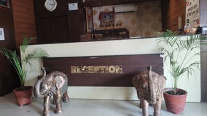 A reception area with a wooden reception desk, two elephant statues, a ceiling fan, and an air conditioning unit. - Hotel Yash Raj (Sihora)