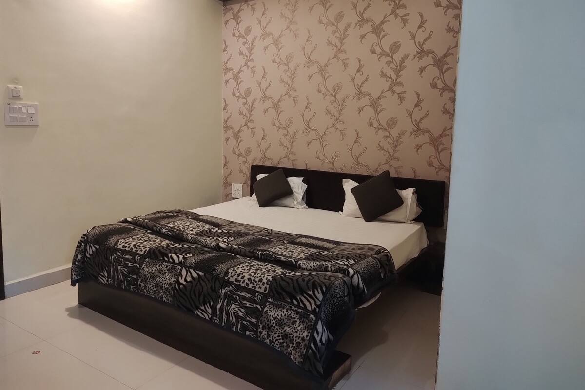 Ein Schlafzimmer mit einem Bett, einer gemusterten Tagesdecke und floralem Wandpapier.