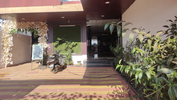 A restaurant entrance with a motorcycle parked outside, a signboard, and a tiled pavement. - Hotel Yash Raj (Sihora)