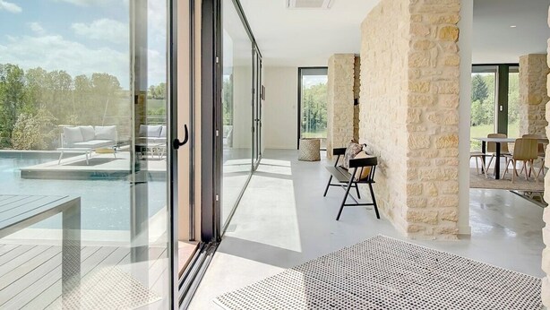 A modern interior with a glass door leading to a pool area, stone walls, and a dining area with outdoor seating. - Villa Molinant, escape in Golden Stones (Bagnols)
