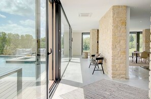 A modern interior with a glass door leading to a pool area, stone walls, and a dining area with outdoor seating. - Villa Molinant, escape in Golden Stones (Bagnols)