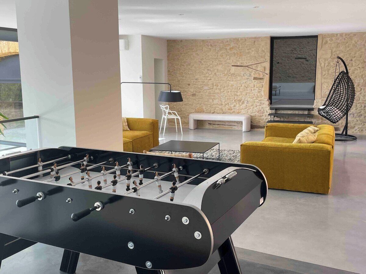 Een moderne woonkamer met een tafelvoetbalspel, een gele bank en een hangstoel.