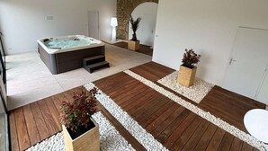 A modern bathroom with a large bathtub, wooden flooring, and a stone archway. - Villa Molinant, escape in Golden Stones (Bagnols)