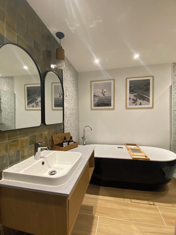 A modern bathroom with a large mirror, two sinks, a bathtub, and framed pictures on the wall.