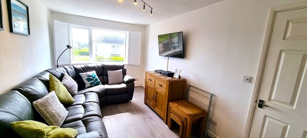 Een woonkamer met een leren bank, een houten kast en een televisie aan de muur.