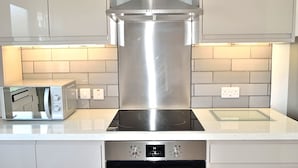 A modern kitchen with stainless steel appliances, a built-in oven, and a microwave on the countertop. - Holiday apartment with direct access to Perranporth beach! (Perranporth)