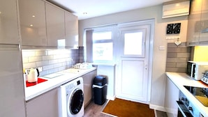A compact kitchen with a washing machine, a trash bin, and a microwave. - Holiday apartment with direct access to Perranporth beach! (Perranporth)