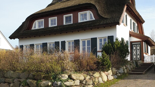 A traditional house with a thatched roof, white walls, and green shutters. It features a stone wall with a rock labeled "60 b" in front. - Island country house SEAside - vacation in a thatched roof house with private beach (Mönchgut)