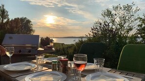 A table set for a meal with plates, cutlery, and glasses, overlooking a body of water with a sunset in the background. - Island country house SEAside - vacation in a thatched roof house with private beach (Mönchgut)