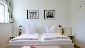 A double bed with white linens, a bedside table with a lamp, and two framed pictures on the wall. - Island country house SEAside - vacation in a thatched roof house with private beach (Mönchgut)