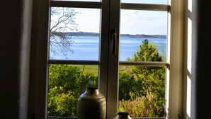 A window with two vases on a sill, overlooking a body of water and greenery. - Island country house SEAside - vacation in a thatched roof house with private beach (Mönchgut)