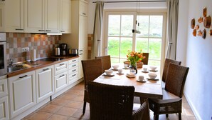 A kitchen with white cabinets, a tiled backsplash, and a dining area with wicker chairs and a table set for four. - Island country house SEAside - vacation in a thatched roof house with private beach (Mönchgut)