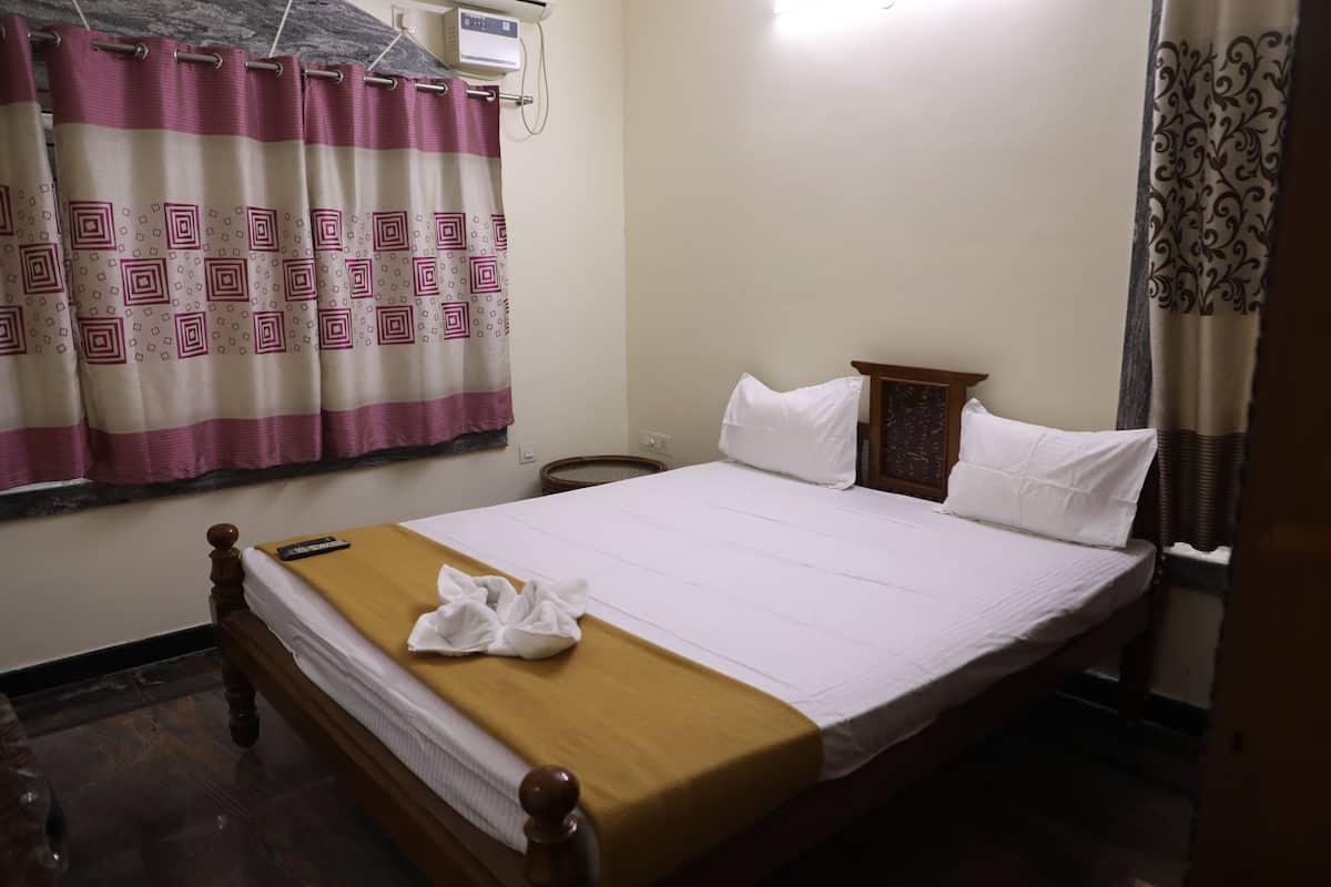 A neatly made bed with a brown bedspread and white pillows, a bedside table with a lamp, and a window with patterned curtains.