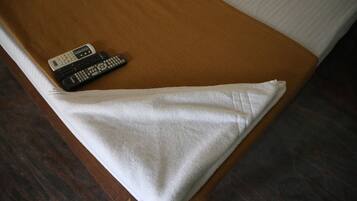 Una cama con cabecera marrón, almohada blanca y dos controles remotos sobre la cama.