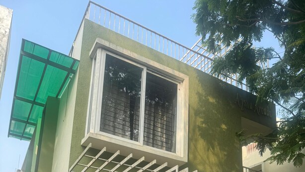 En boligbygning med en grøn facade, en balkon med gelænder og en trappe med gelænder samt en rød dør.