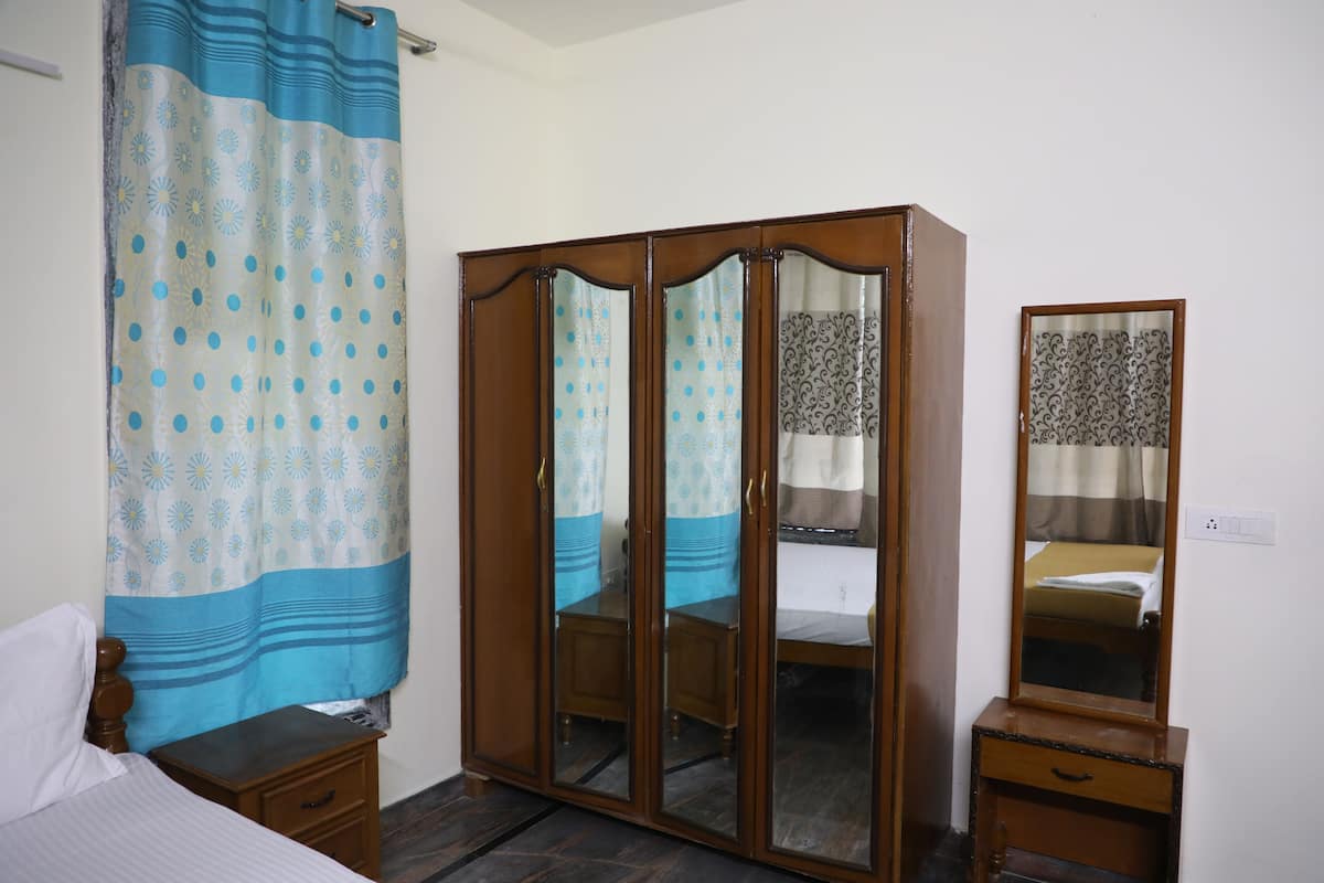 A bedroom with a bed, a wooden wardrobe, a bedside table, and a mirror.