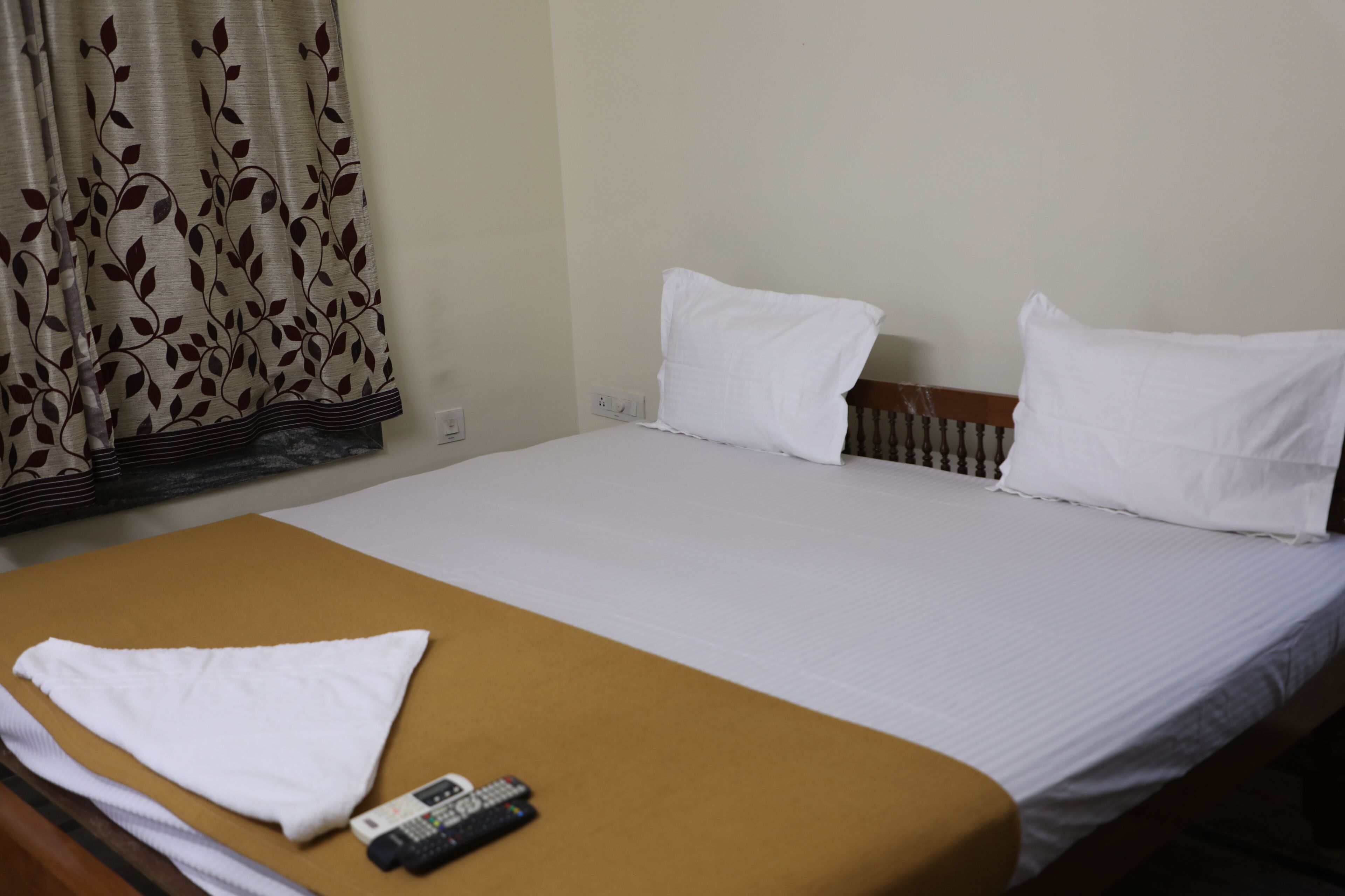 A hotel room with a bed, a brown bedside table, a remote control, and a white towel.