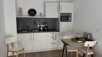 Une cuisine moderne avec des meubles blancs, un plan de travail noir, un four à micro-ondes, une machine à café et un grille-pain. Il y a deux chaises et une table.