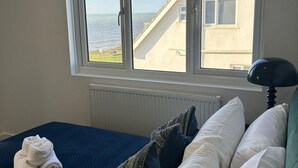 A bedroom with a bed, a window with a view of a building and the sea, and a radiator. - Ocean Side With Free Parking By My Getaways (Peacehaven)