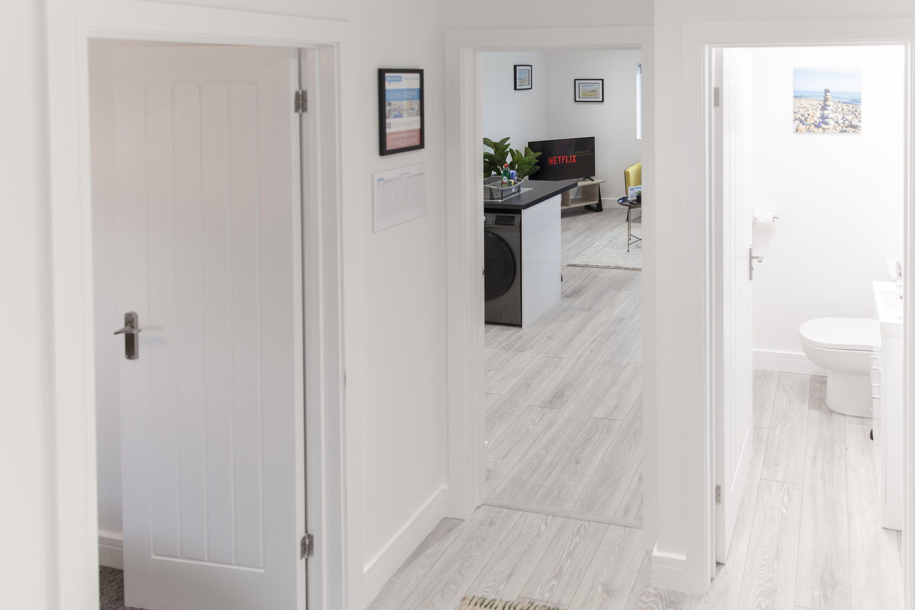 Un couloir d’hôtel moderne donnant sur un coin cuisine, une salle de bain et un salon équipé d’un téléviseur.