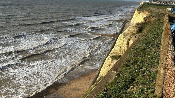 A coastal view with a sandy beach, a concrete sea wall, and a row of houses in the background. - Ocean Side With Free Parking By My Getaways (Peacehaven)