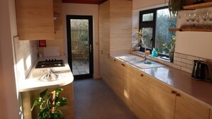 A modern kitchen with wooden cabinets, a gas stove, a sink, and a window with a view of greenery. - Lovable Lancing With Garden Parking (Lancing)