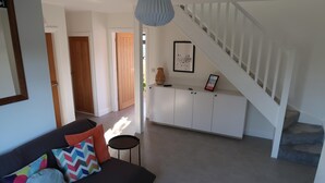 A modern living room with a dark sofa, colorful cushions, a small round table, and a staircase leading to another room. - Lovable Lancing With Garden Parking (Lancing)