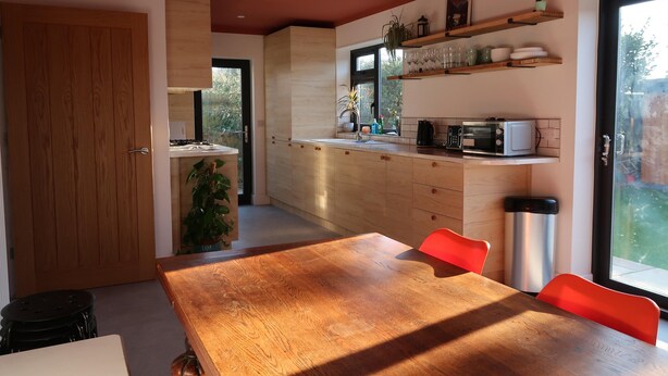 A modern kitchen with wooden cabinets, a dining table with chairs, and a window providing a view of the outdoors. - Lovable Lancing With Garden Parking (Lancing)