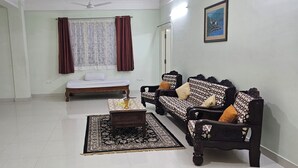 Una sala de estar con un conjunto de sofá, una mesita, una cama y una ventana con cortinas.