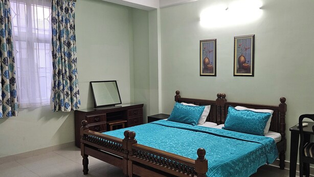 Un dormitorio con cama, mesita de noche, una silla y una ventana con cortinas.
