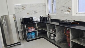 Una cocina con un refrigerador de acero inoxidable, un microondas y una estufa a gas. Hay repisas con ollas y sartenes, y una ventana con vistas.