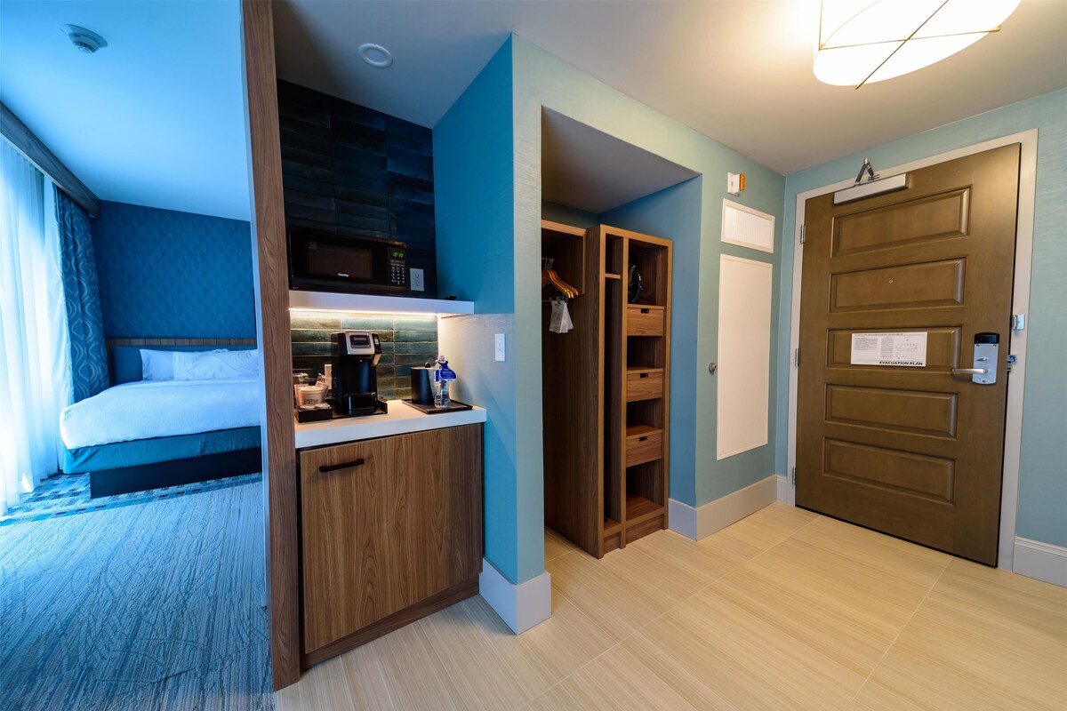 Habitación de hotel con cama, kitchenette, armario y puerta con un letrero.