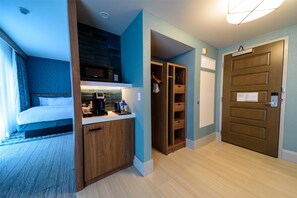 Habitación de hotel con cama, kitchenette, armario y puerta con un letrero.
