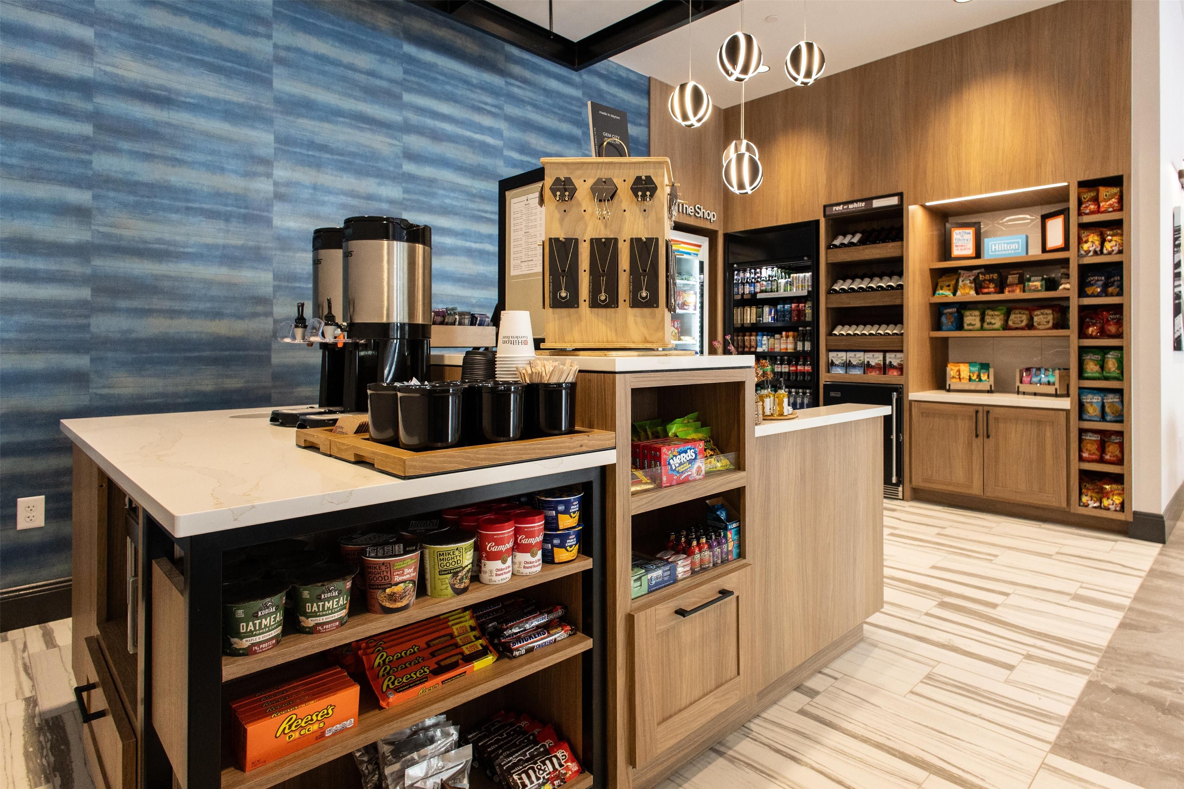 A modern kitchen area with a coffee station, shelves stocked with snacks, and a wooden counter.