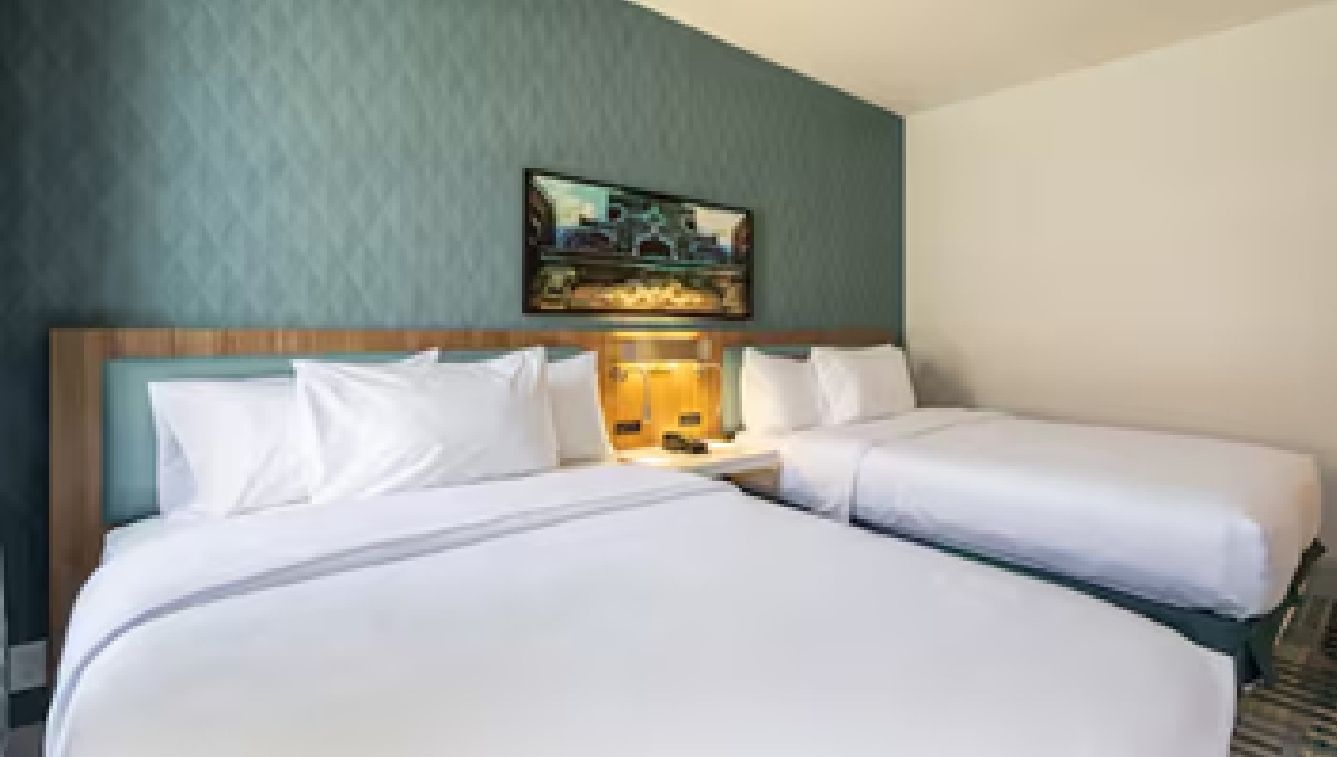 A hotel room with two beds, a headboard, a nightstand, and a painting on the wall.