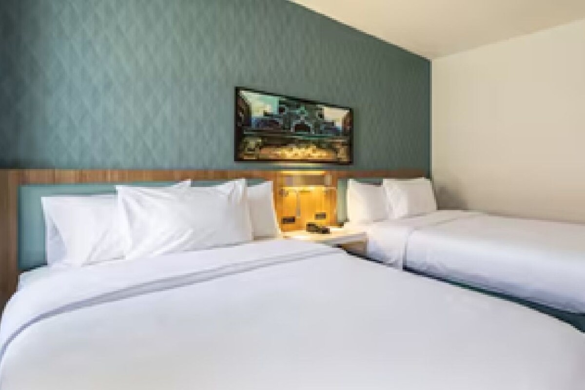 A hotel room with two beds, a headboard, a nightstand, and a painting on the wall.