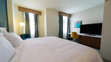 A hotel room with a large bed, a desk with a television, a chair, and curtains.