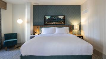 A hotel room with a large bed, a desk with a lamp, a chair, and a painting on the wall.