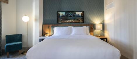 A hotel room with a large bed, a desk with a lamp, a chair, and a painting on the wall.