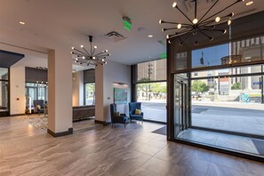 A modern lobby with a large glass door, a seating area with chairs, and a unique ceiling light fixture. - Hilton Garden Inn Dayton Downtown (Dayton)