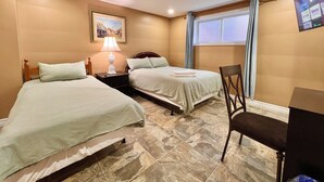 Une chambre d’hôtel avec deux lits, une table de chevet avec une lampe, une chaise, un téléviseur fixé au mur et une fenêtre avec des rideaux.