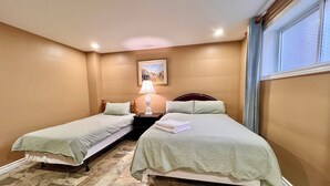 Une chambre d’hôtel avec deux lits simples, une table de chevet avec une lampe, un tableau au mur et une fenêtre avec des rideaux.