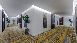 A hallway with a patterned carpet, white walls, and framed artwork. - Garden Millennium Hotel Suites - Alsewes (Jizan)
