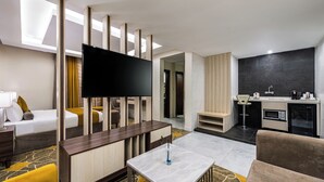 A modern hotel room with a flat-screen TV, a dining area, a kitchen, and a separate living area with a sofa and armchairs. - Garden Millennium Hotel Suites - Alsewes (Jizan)