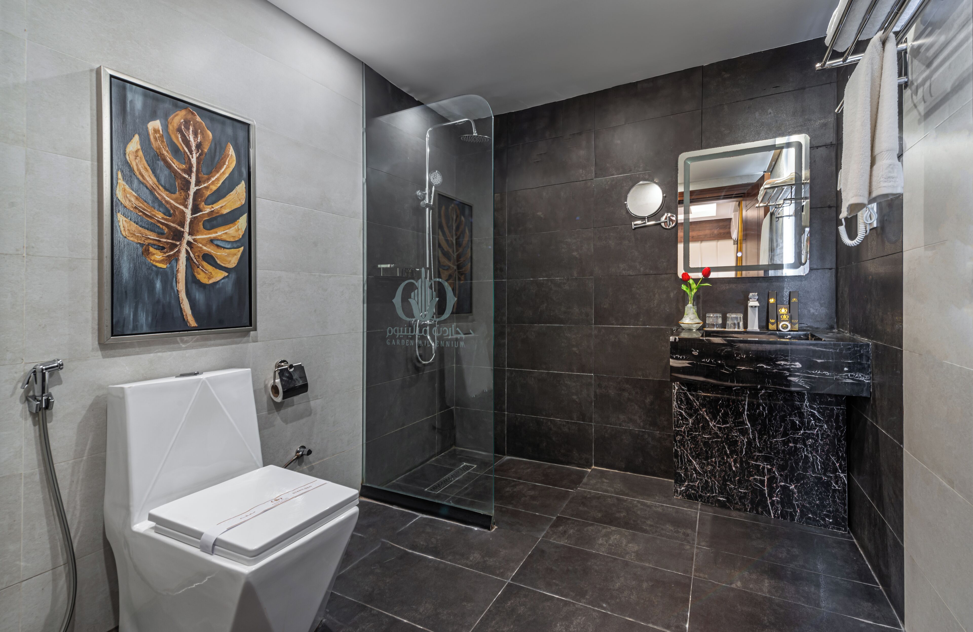A modern bathroom with a glass-enclosed shower, a white toilet, a marble sink, and a large leaf artwork on the wall.