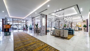 A modern hotel lobby with a marble reception desk, seating area, and glass partitions. - Garden Millennium Hotel Suites - Alsewes (Jizan)