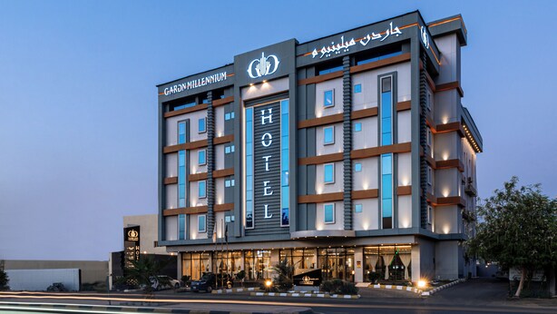 A multi-story hotel with a prominent 'HOTEL' sign, featuring a modern architectural design with a mix of glass and concrete, and a well-lit entrance. - Garden Millennium Hotel Suites - Alsewes (Jizan)