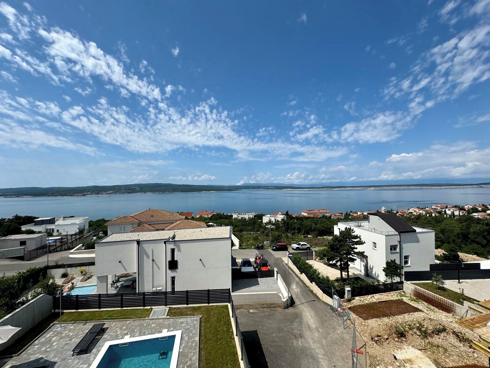 A modern residential area with a swimming pool, white buildings, and a view of a large body of water.