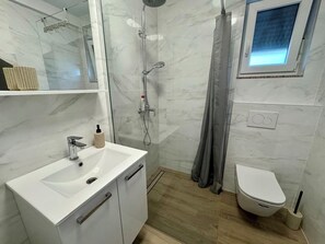 Een moderne badkamer met een witte wastafel, douche en toilet.
