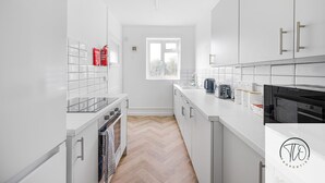 A modern kitchen with white cabinetry, a herringbone wood floor, a window, and a view of trees outside. - 4BR House | Near Sizewell (Peasenhall)